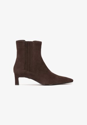 Hnedé semišové členkové topánky s ostrou špičkou a nízkym podpätkom. Vertikálne elastické panely po bokoch zvyšujú flexibilitu a pohodlie pri nosení.