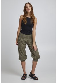 Pantaloni cropped verde oliva con polsini elastici, caratterizzati da una vita arricciata, abbinati a un top senza maniche nero e sandali neri.