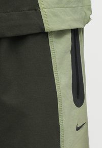 Nike-shorts met een dual-tone ontwerp in lichtgroen en donkerolijfgroen stof. Inclusief een zwarte ritszak en gestikte accenten.