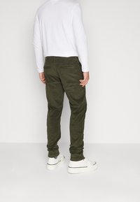 Gröna kordflorsbyxor med rak passform, två bakfickor, kombinerat med en vit långärmad skjorta och vita sneakers.