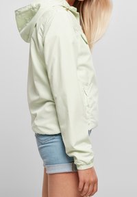 Lys grøn, letvægts hættetrøje med elastiske manchetter, centralt lynlås og sidelommer, parret med denimshorts.