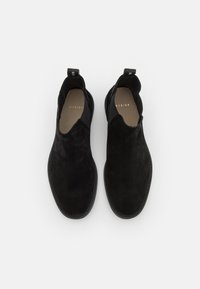 Chaussures noires en daim à enfiler avec une texture lisse, bout arrondi, panneaux latéraux élastiques et une languette à l'arrière. Design minimaliste sans matériel visible.