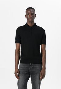 Svart polo skjorte med korte ermer og knapper, laget av et glatt, lett materiale, kombinert med mørkegrå jeans.