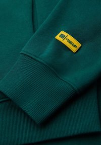 Felpa verde con polsini a costine, caratterizzata da un'etichetta rettangolare gialla prominente con il testo "LEVEL UP". Tessuto morbido.