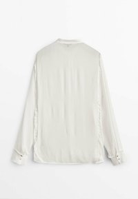 Blouse blanche à manches longues avec plis discrets, poignets boutonnés et encolure ronde, vue de dos sur fond blanc.