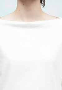 Hvit topp med korte ermer og bred, båtformet halsutringning. Glatt, lett stoff med enkelt design uten synlige mønstre eller pynteelementer.