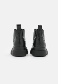 Stivali alla caviglia in pelle nera con finitura liscia, punta arrotondata, linguette per il pull e suole nere spesse. Design minimalista e costruzione senza soluzione di continuità.