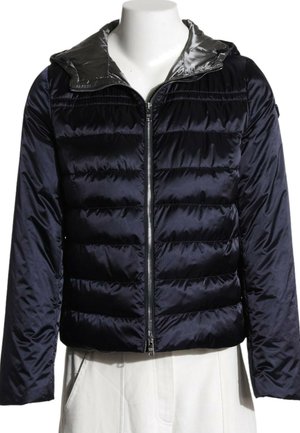 Doudoune noire brillante avec matelassage horizontal, fermeture éclair frontale et capuche portée sur un pantalon blanc sur un mannequin sans tête.