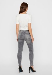 Jeans ajustados de mezclilla gris con una textura desgastada, combinados con una blusa blanca entallada. El conjunto se completa con zapatos de tacón alto negros.