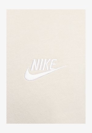 Logo de Nike sobre un fondo de tela beige claro. El logo está bordado en blanco, presentando una tipografía limpia y un diseño de swoosh.