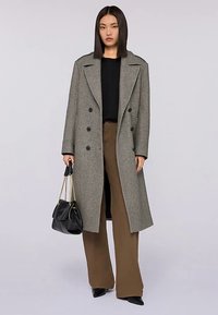 Dwurzędowy szary płaszcz wełniany z szerokimi klapami, czarny dziany top, brązowe spodnie o szerokich nogawkach oraz czarna torebka ze złotymi akcentami.