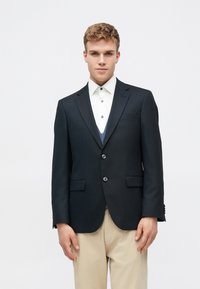 Tume mere blazer kahe nööbiga, servalapid ja ees taskud. Kantud valge särgi peale, millel on peen sinine aktsent. Beez püksid.