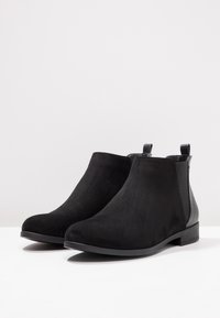 Botines de ante negro con puntera redondeada, paneles laterales texturizados y lengüetas para facilitar su uso. Suelas planas que ofrecen un diseño casual y minimalista.