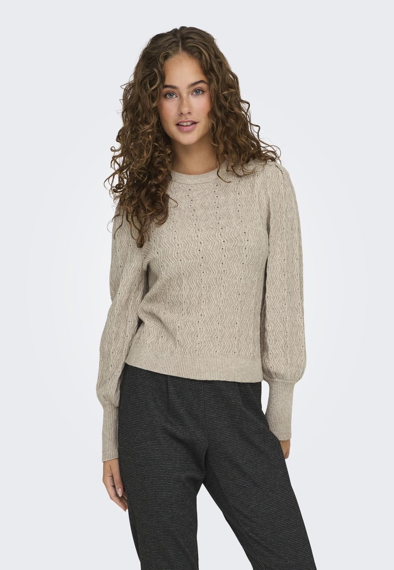 Pull en maille beige avec un motif de vagues texturé et de petits œillets, doté de longues manches bouffantes et d'un col rond simple.