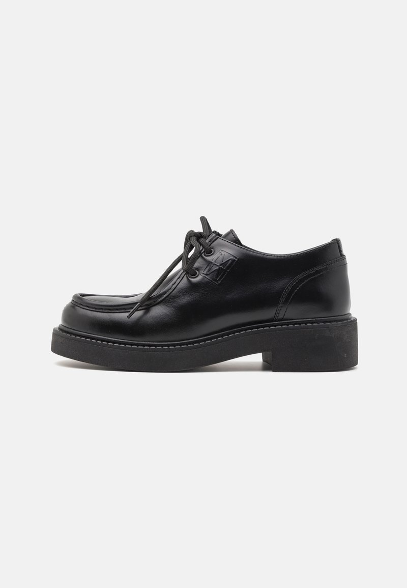 Chaussures en cuir noir avec un bout arrondi, un design à lacets, une semelle épaisse noire et des coutures tonales. Un petit logo est visible sur le côté.