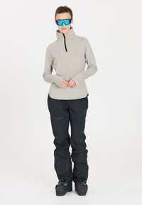 Lichtgrijs, vochtafvoerend shirt met een ritskraag en zwarte broek met ritszakken. Zwarte skischoenen maken de outfit compleet.