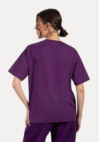 T-shirt in cotone viola con maniche corte, colletto tondo e vestibilità rilassata, caratterizzata da una texture liscia e un design semplice.