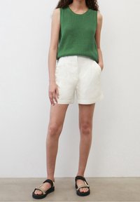 Green textured sleeveless top, white shorts with side pockets, and black sandals with gold accents. Simple and casual design.