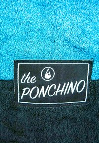 Sininen froteekangas, jossa on musta etiketti, jossa lukee "the PONCHINO" valkoisella tekstillä, ja brändin nimen yläpuolella on pisara-logo.