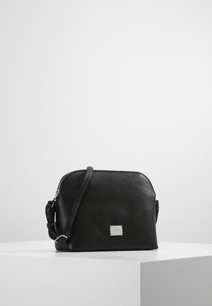 Musta teksturoitu nahkainen olkalaukku hopeisella vetoketjulla ja säädettävällä hihnalla, esillä valkoisella jalustalla yksinkertaisen taustan edessä.