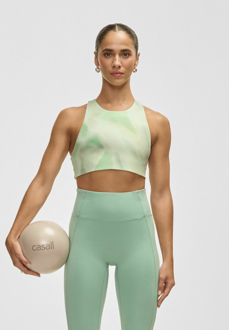 Ljusgrön sportcroptop med vågigt mönster, tillsammans med högmidjade mintgröna leggings. Håller en beige fitnessboll märkt 'casall'.