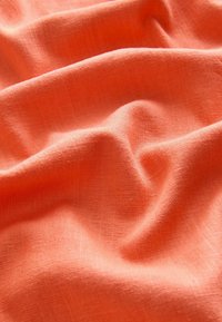 Tessuto arancione leggero con una superficie leggermente texturizzata, che mostra morbide pieghe e drappeggi, tipici dei materiali come lino o cotone.