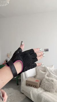 Fekete félujjas kesztyűk texturált fogással, rózsaszín díszítésekkel és csuklópánttal. Az ujjak szabadon vannak; részletes mintázatok javítják a tapadást.