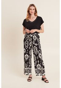 Zwarte V-hals top gecombineerd met wijdvallende, hoogwaterbroeken met een gedurfde witte print. Model draagt zwarte hoge hakken.