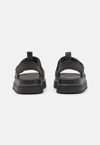 Svart sandaler med teksturert gummi såle og justerbare stropper. Minimalistisk design med bakre trekkflik for enkel bruk.