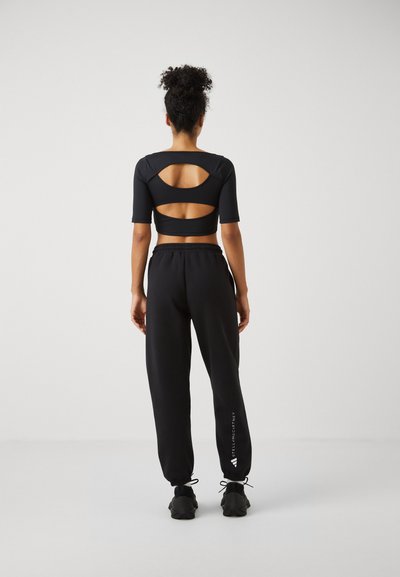 Black cropped top with short sleeves features cut-out designs on the back. Paired with loose-fitting black sweatpants with logo detail.