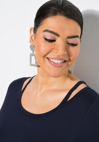 Mörkblå topp med rundad halsringning; stora silvriga örhängen med en rund sten och rektangulära hängande former, täckta med rhinestones.