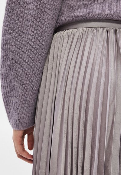Gros plan sur un pull à manches longues en tricot lavande et une jupe plissée taille haute assortie dans une nuance de violet clair.