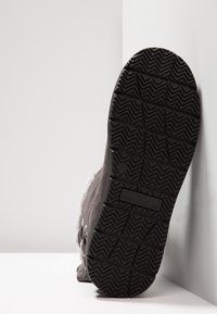 Bota negra texturizada con suela de goma gruesa, que cuenta con un suave forro interior y acentos de hardware en los laterales. El diseño es elegante y funcional.