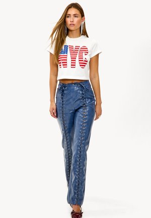 T-shirt blanc court avec le texte "NYC" en rouge et bleu, assorti à un pantalon en cuir bleu brillant avec des détails de lacets sur le côté et des zips.