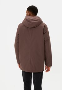 Giacca impermeabile marrone con cappuccio, caratterizzata da una superficie liscia e un taglio dritto, cuciture visibili e un design semplice.