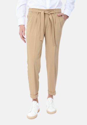 Pantaloni beige con vita legata, davanti plissettato e orli arrotolati, abbinati a sneakers bianche con suola beige.