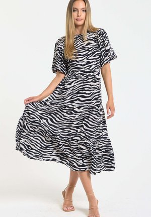 Woman wearing a black-and-white zebra print midi dress with puff sleeves, holding the skirt, and beige strappy heels.