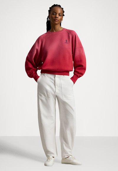 Rød genser med gradientdesign, rund hals og raglanermer. Kombinert med løse hvite bukser og lette sko.