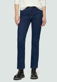 Granatowe dżinsy o dopasowanym kroju, wykonane z denimu. Posiadają pięć kieszeni i delikatne detalowanie za pomocą ściegów. W połączeniu z czarnymi botkami za kostkę.