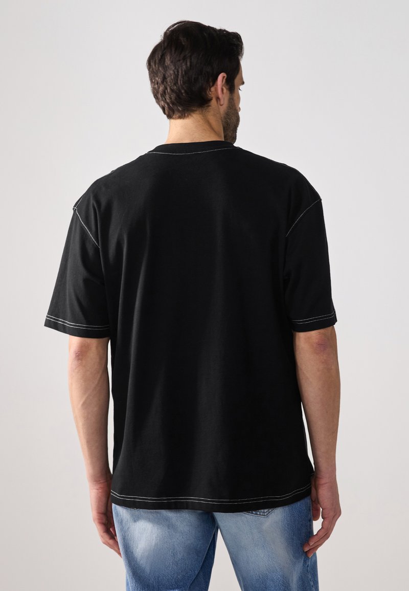 T-shirt noir à manches courtes en coton avec des détails de couture contrastés. Coupe décontractée, encolure ronde et dos uni.