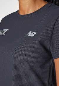 T-shirt atlético azul-marinho feito de tecido leve; apresenta riscas subtis e um logo refletor da New Balance na parte da frente.