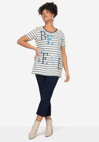 Gestreifte T-Shirt mit kurzen Ärmeln, ausgestattet mit blauer Schrift. Kombiniert mit marineblauen Hosen und beigen Stiefeletten. Sanfter Stoff, lockere Passform.