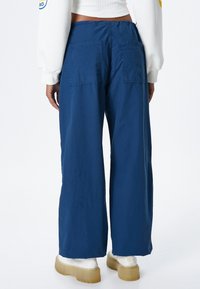 Wijduitlopende broek van marineblauwe stof, met twee achterzakken en een relaxte pasvorm, gecombineerd met chunky witte en doorzichtig beige schoenen.