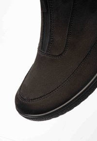 Nahaufnahme der Vorderkappe eines schwarzen Wildlederstiefels mit sichtbaren Nähten und strukturierter Gummisohle vor weißem Hintergrund.