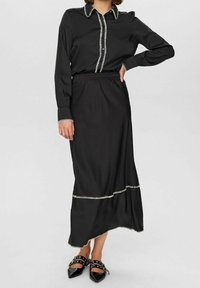 Černá blůza s kontrastním bílým šitím a límečkovým výstřihem, spárovaná s černou sukní ke kolenům s vrstveným designem a lemováním.