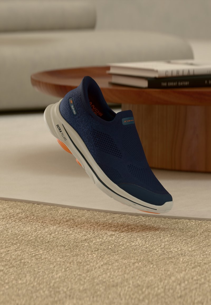 Οι ναυτικές πάνινα παπούτσια τύπου slip-on διαθέτουν επάνω μέρος από δίχτυ για αναπνοή, λευκή εξωτερική σόλα με πορτοκαλί λεπτομέρειες και ελαφρύ σχεδιασμό για άνεση.