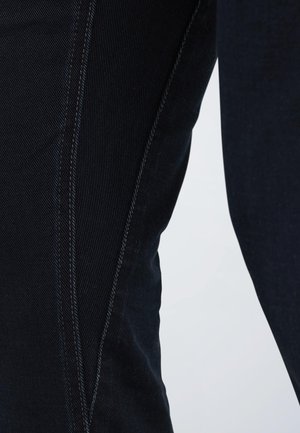 Jean en denim foncé présentant un design ajusté avec des coutures contrastées le long des coutures, mettant en valeur un tissu lisse et texturé.
