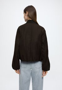 Sort bomberjakke med cropped silhuett, elastisk midjebånd og voluminøse ermer, kombinert med lyseblå høytlivs jeans.