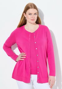 Rosa kofta i slätstickad kvalitet med rund halsringning, framknäppning och långa ärmar. Matchas med en matching topp och vita byxor.