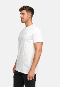 White cotton t-shirt with a crew neck, short sleeves, and a small logo on the chest, paired with black cargo pants.